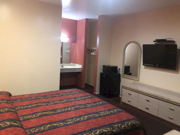 A hotel room with two double beds, a long dresser, wall mirror, flat-screen TV, and a small vanity area near the bathroom.