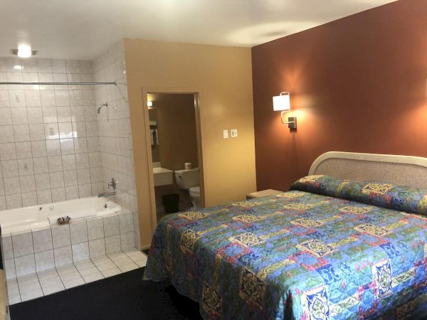 A hotel room with two queen beds covered in colorful quilts, a maroon accent wall with bedside lamps, and an adjacent tiled bathroom area.
